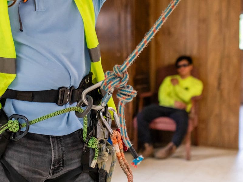Climber's harness with carabiners and ropes, worker resting in background.