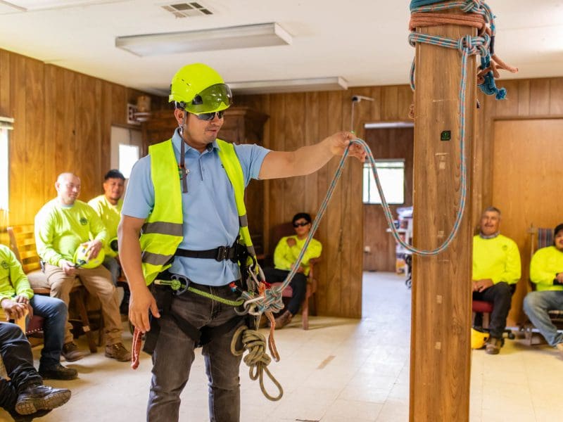 Construction workers in safety gear working indoors with ropes and harnesses.