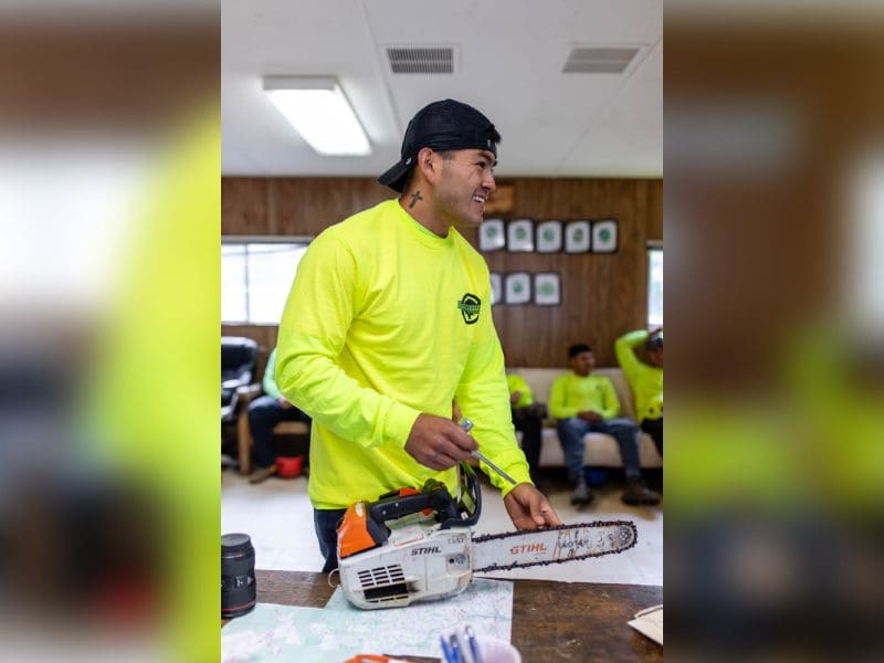 Man in yellow shirt handling a chainsaw indoors.