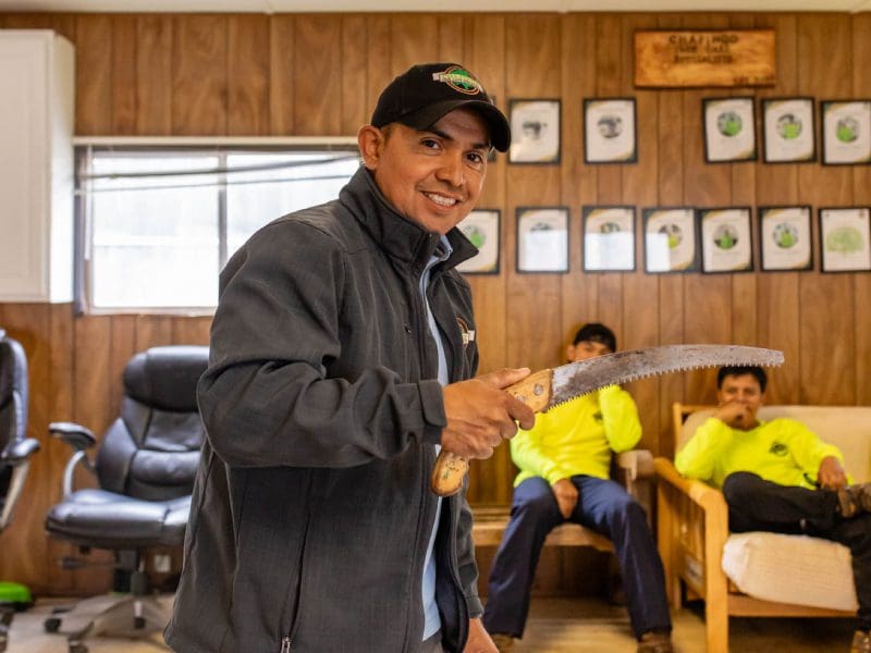 Smiling man giving a thumbs up in a cozy room with two seated people.